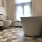 Badkamer in jaren '30 woning met een vrijstaand bad, kleurrijke hexagonale vloertegels en een strakke, moderne wastafel.