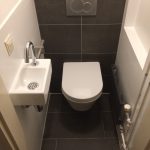 Klein toilet met strakke grijze tegels, moderne inbouwspoeling en een compacte wandwastafel.
