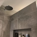 Luxe inloopdouche met grote grijze tegels, een regendouchekop en een ingebouwde nis voor shampoo en accessoires.