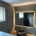 Moderne badkamer met een zwart-witte waskom, grote spiegel met sfeerverlichting en strakke betonnen tegels.