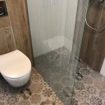 Charmante badkamer met een moderne inloopdouche met glazen wand, een strakke, zwevende toiletpot en een prachtige mozaïektegelvloer die de ruimte een unieke, stijlvolle uitstraling geeft.