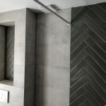 Inloopdouche met grijze betonlook tegels, een chevron patroon op de muur en een ingebouwde nis voor extra opbergruimte.
