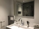 Strakke badkamer met dubbele wastafel, moderne kranen, en een spiegel die de inloopdouche reflecteert.