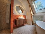 Badkamer in oude woning met vrijstaand bad, houten wastafelmeubel, terracotta tegels en dakraam voor natuurlijk licht.