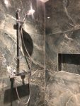 Luxe inloopdouche met marmeren wandtegels, een moderne doucheset met handdouche en ingebouwde nis voor extra opbergruimte.