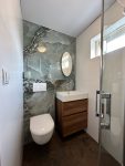 Moderne badkamer met marmeren wandtegels, zwevend toilet, houten wastafelmeubel en een grote spiegel.