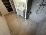 Badkamer met vernieuwde vloer en douchehoek na lekkage, afgewerkt met neutrale tegels en een strak wastafelmeubel.