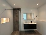 Ruime badkamer op de 17e verdieping met inloopdouche, moderne wastafel met dubbele kranen en strakke zwarte accenten.