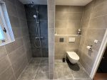 Strakke badkamer met inloopdouche, zwevend toilet en grote tegels die de ruimte open en licht maken.