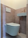Moderne toiletrenovatie met een zwevend toilet, roestkleurige wateraansluiting en zachte roze wandtegels en groene sanitair