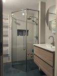 Moderne badkamer met inloopdouche met glazen wanden, houten wastafelmeubel en ronde spiegel, gelegen in een woning in Leusden.