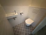 Toilet met witte wandtegels, een moderne fontein, een zwevend toilet en een kleurrijke mozaïektegelvloer voor een frisse uitstraling.